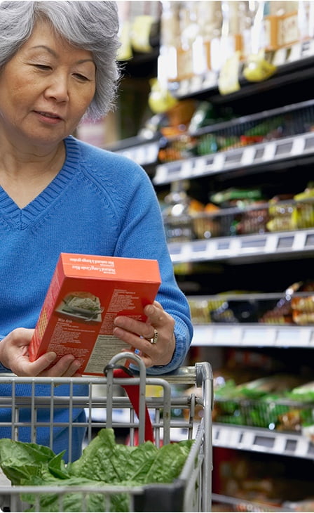 Personne à l’épicerie lisant les ingrédients sur l’emballage d’un aliment transformé.
