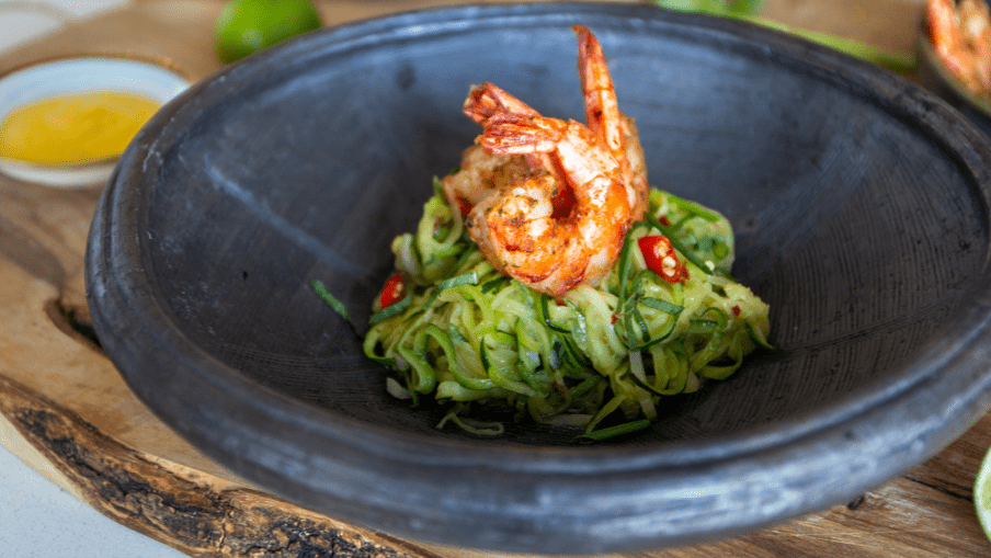 Cooked shrimp on top of zucchini noodles in a bowl with mango sauce on the side. Cooked shrimp on top of zucchini noodles in a bowl with mango sauce on the side.