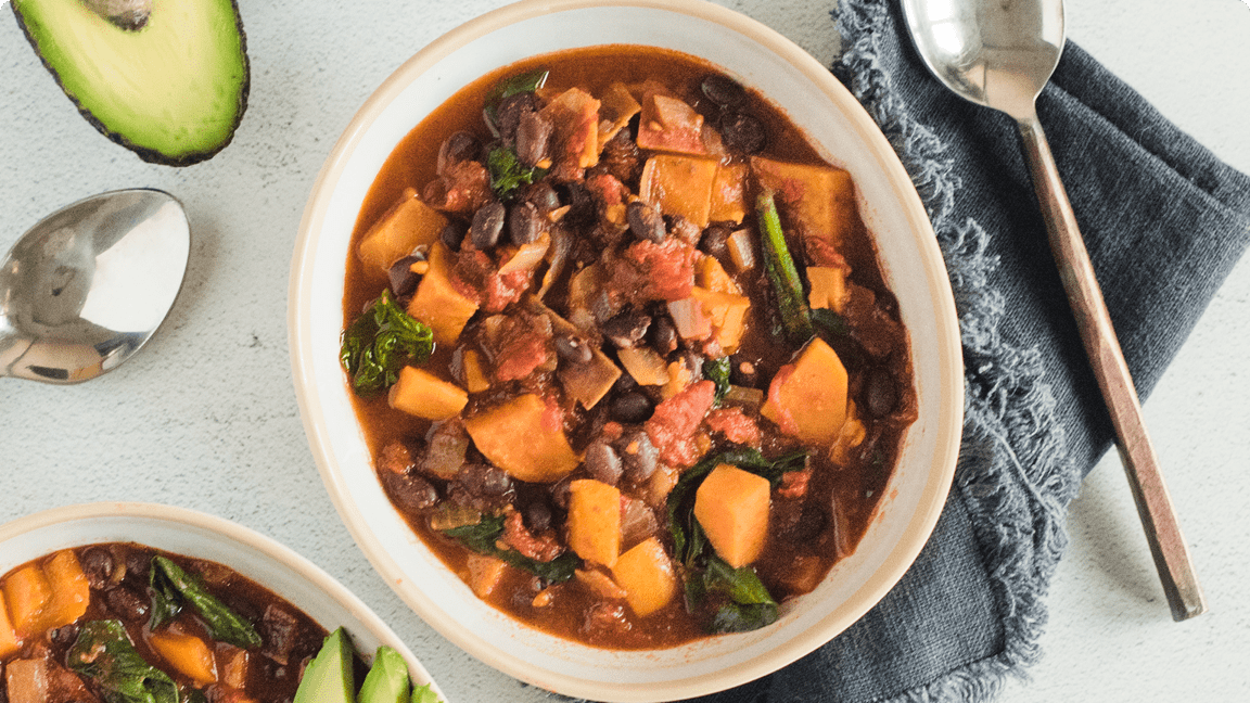 Sweet potato and black bean chilli in a bowl with garnish ready to be served. Sweet potato and black bean chilli in a bowl with garnish ready to be served.